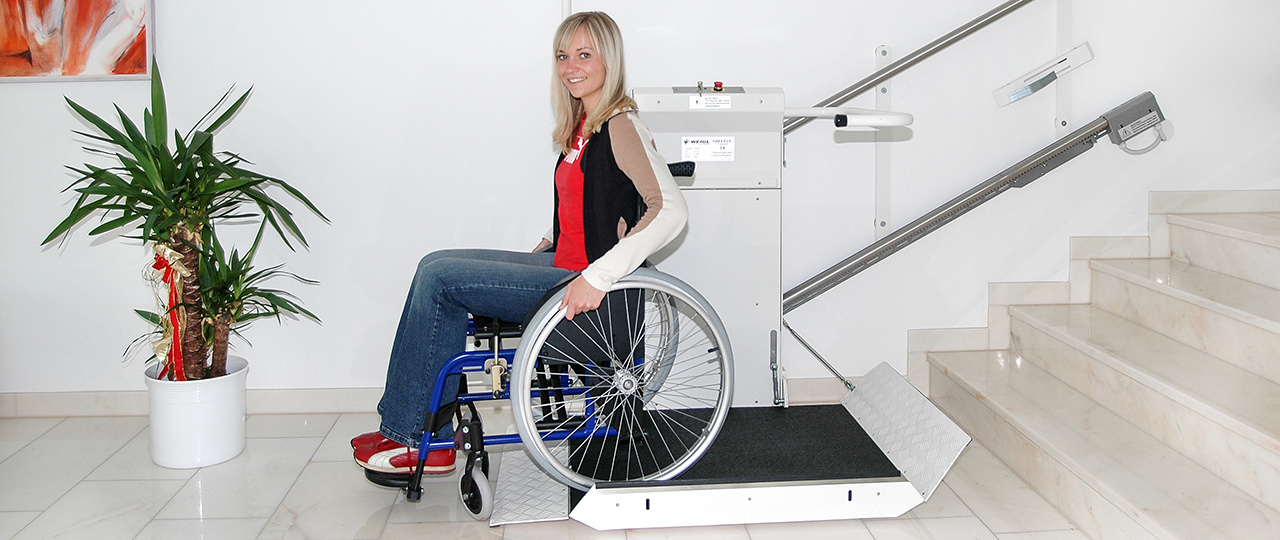 Eine junge Dame benutzt mit ihrem Rollstuhl den Plattformtreppenlift